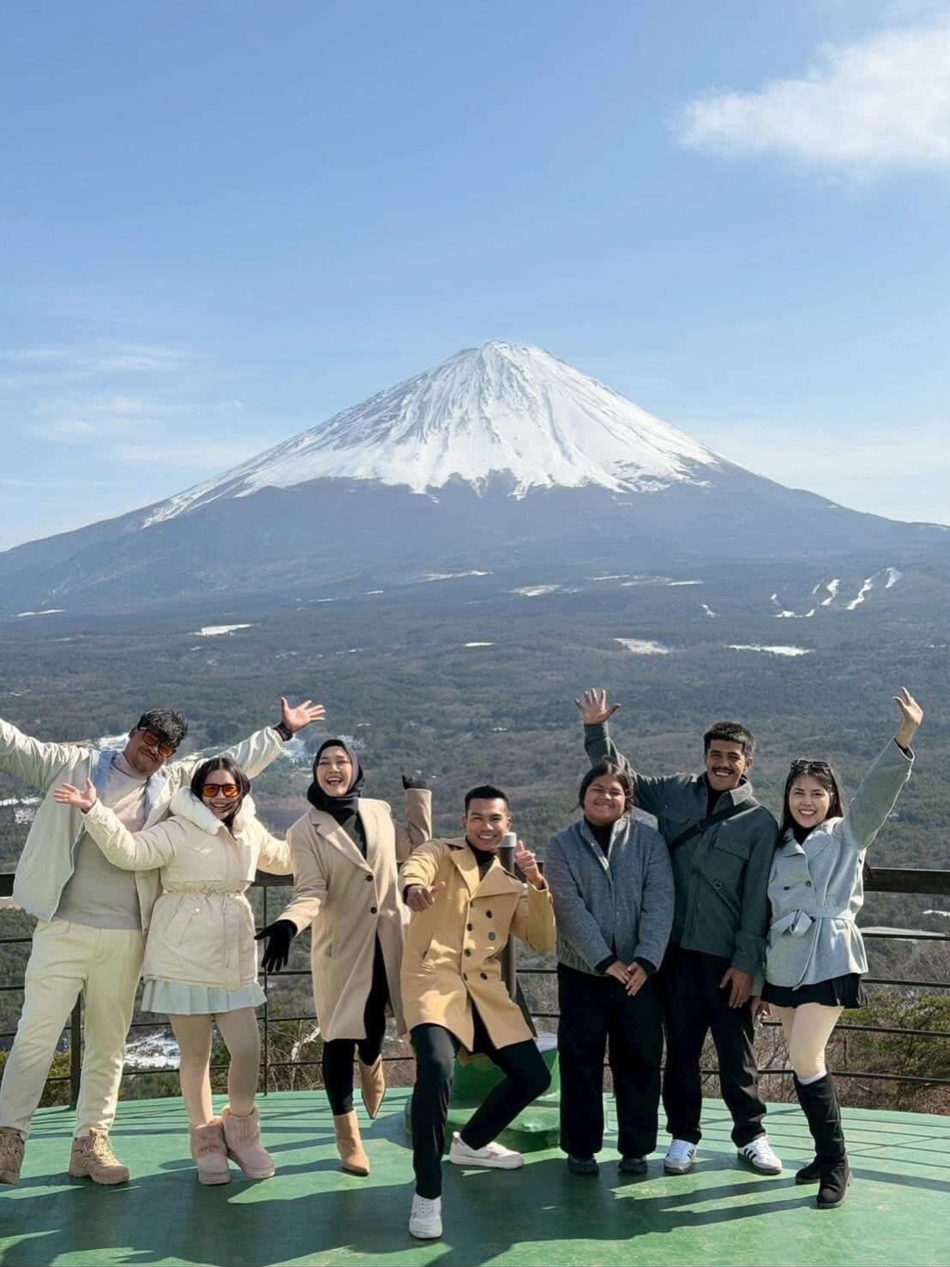 A group of guests cheering with arms raised in front of snow-capped Mt. Fuji