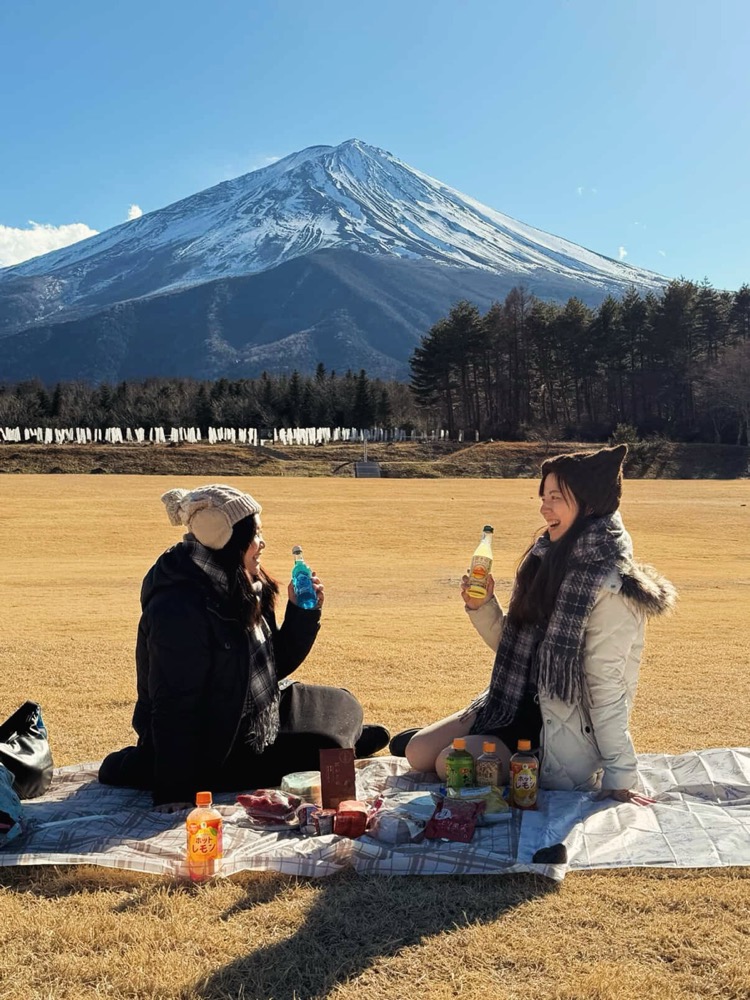 Two friends laughing at a picnic with Mt. Fuji behind them