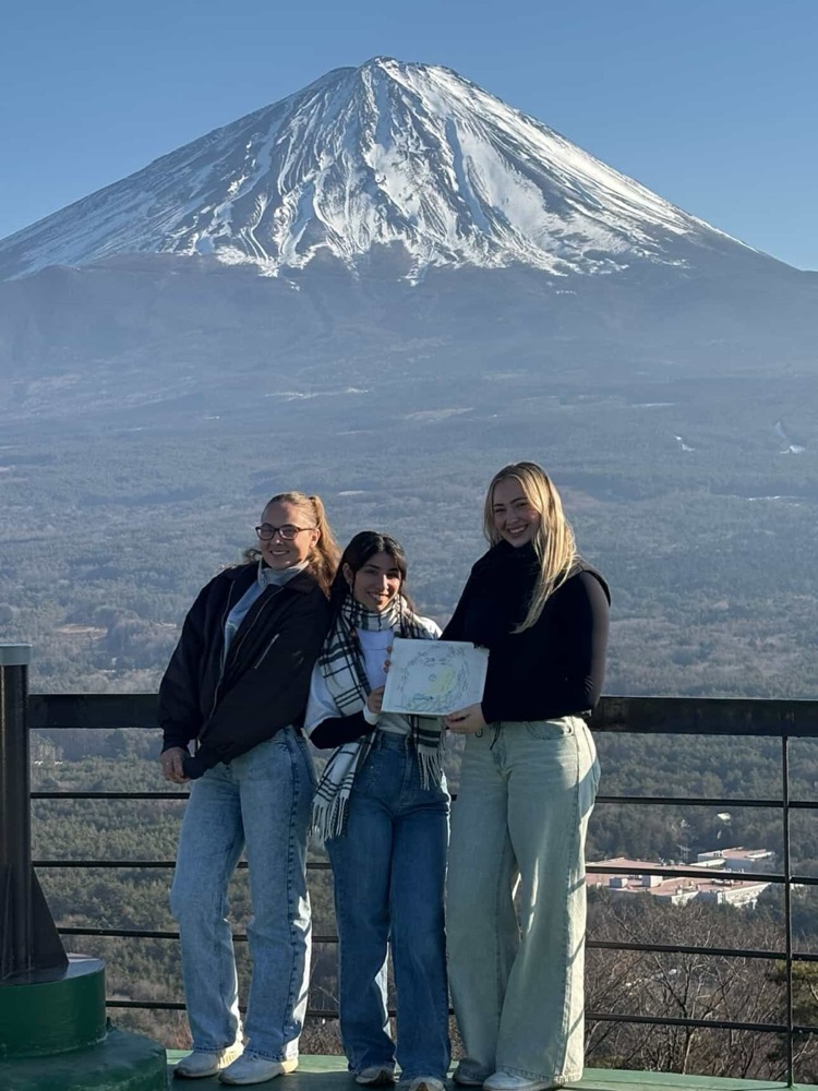 Three friends smiling at a viewpoint in front of Mt. Fuji