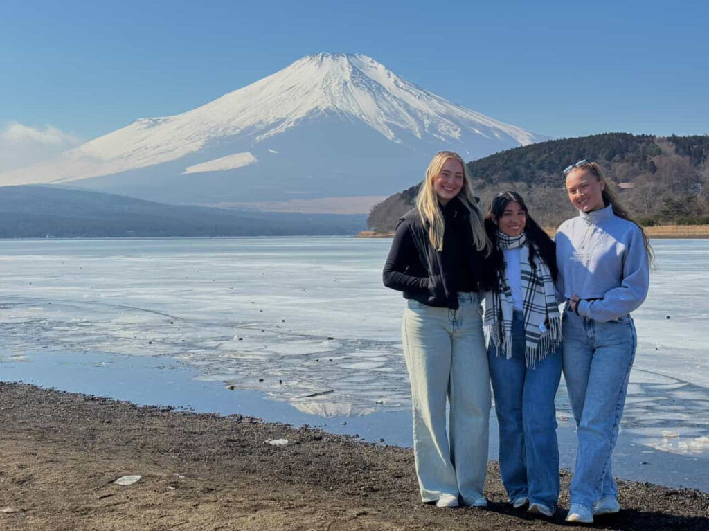 Three guests by a quiet, partly frozen lake with snow-capped Mt. Fuji