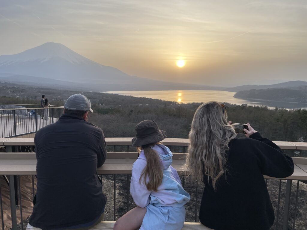 A family at a viewpoint watching the sun set over a lake beside Mt. Fuji
